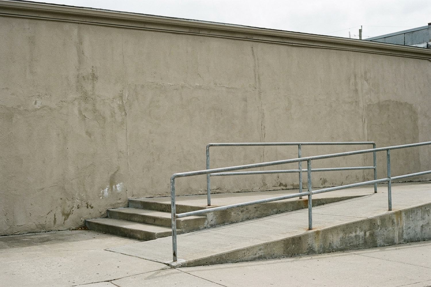 A gently rising concrete ramp beside three shallow steps, with a metal handrail.